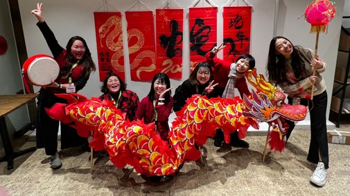 Five people, all smiling and posing, holding a large, red Chinese dragon puppet